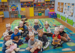 Dzieci siedzą na dywanie ze swoimi maskotkami.